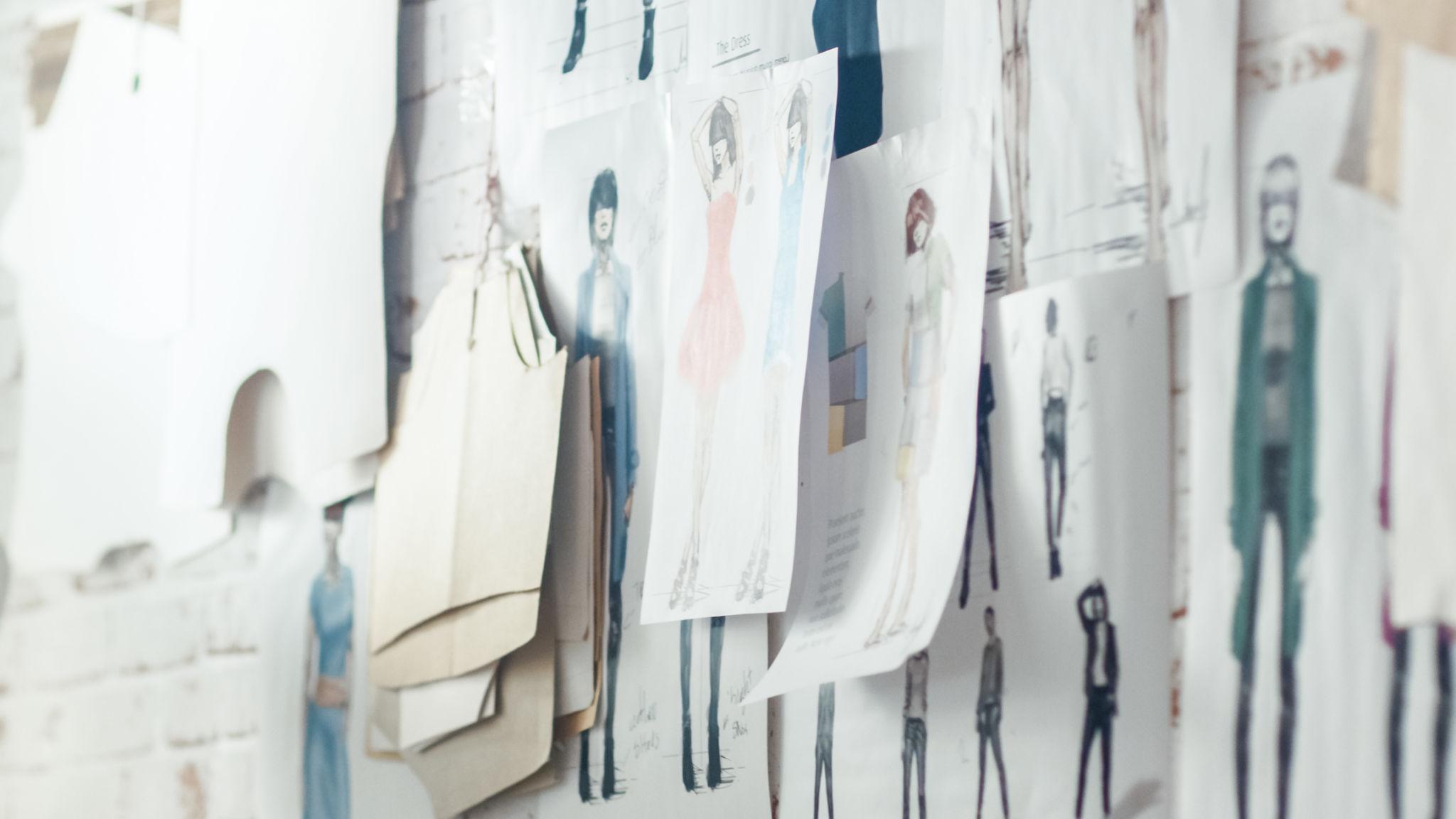 Fashion sketches and material studies pinned on a studio wall