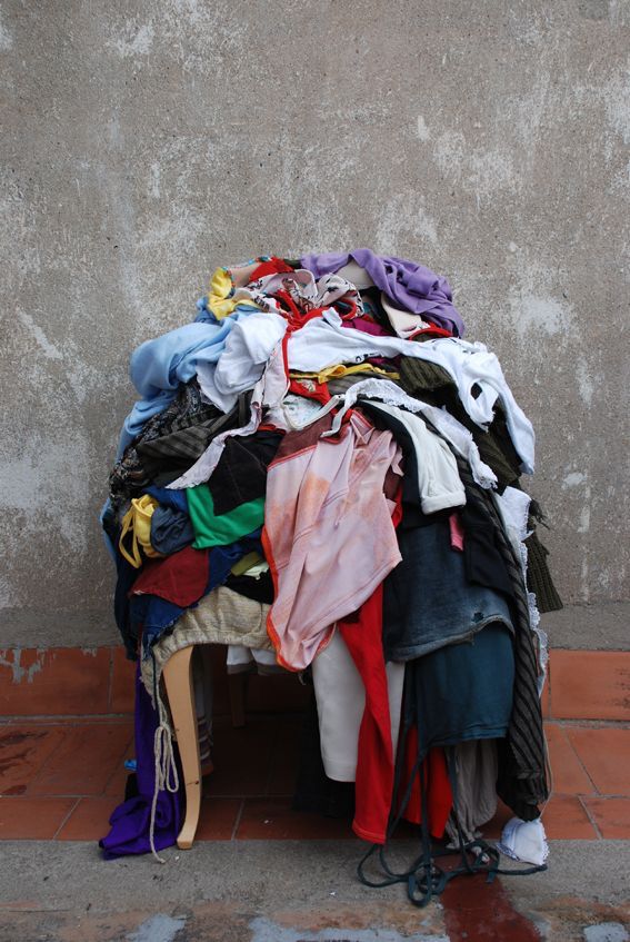 Discarded clothing piled on a chair against a concrete wall